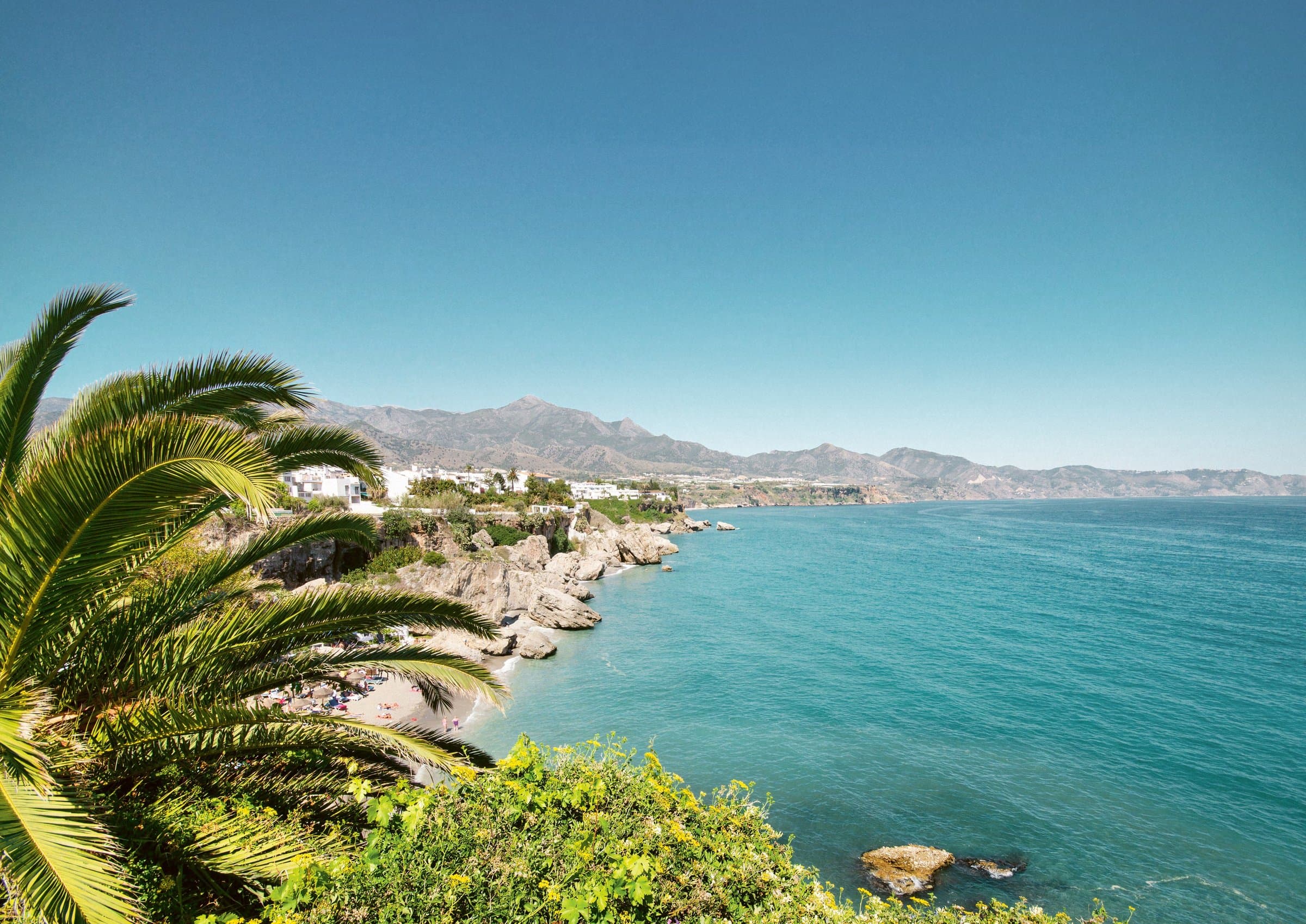 Spaanse kustlijn met palmen, een baai en bergen aan de horizon